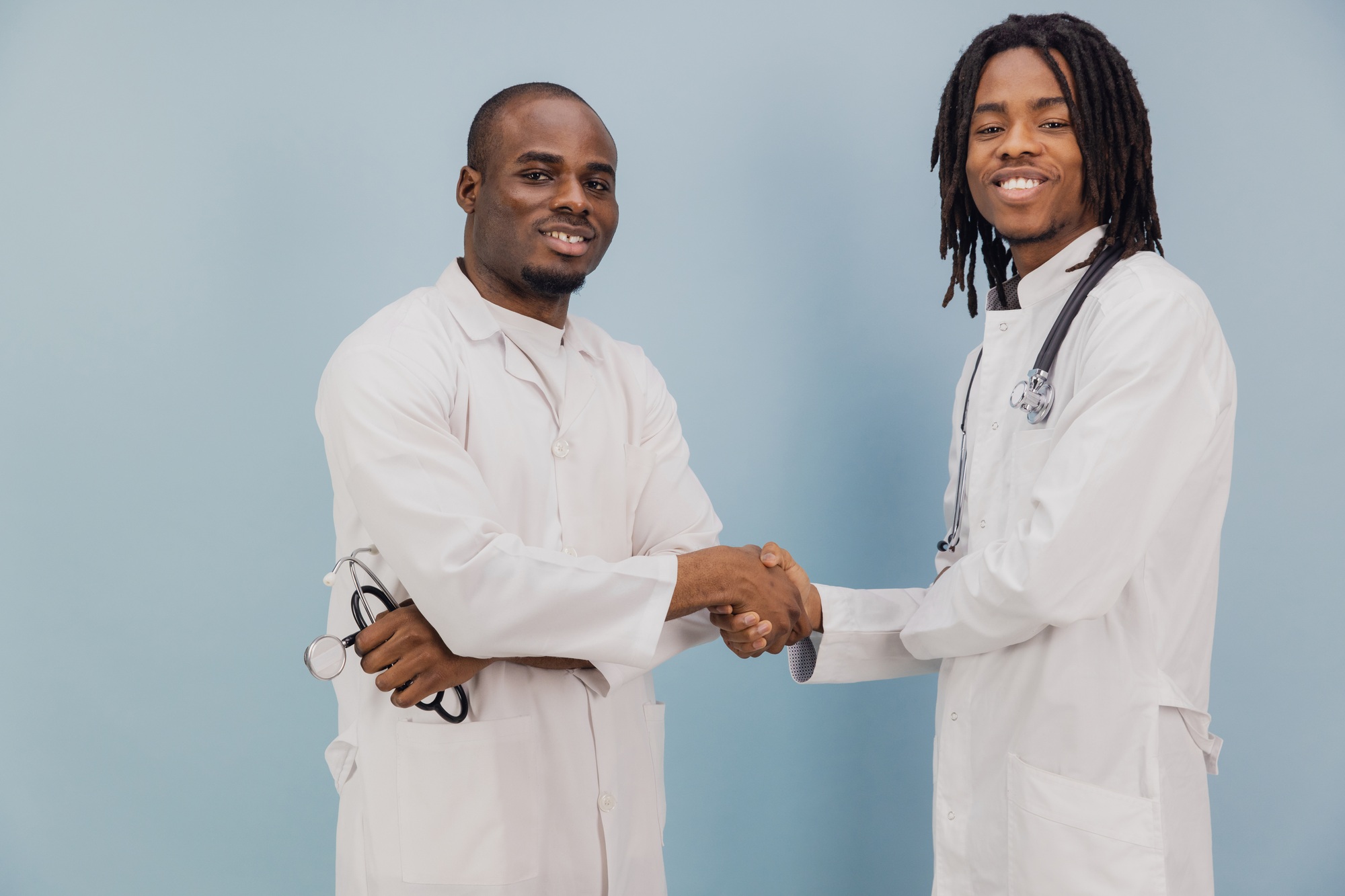 Two Young African American Doctors Shaking Hands on Blue Background